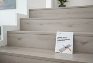 Close-up of a newly installed modern staircase with light grey wood-look vinyl or laminate flooring, with a leaflet or manual entitled 'Perfect Stairs: Easy Vinyl Flooring Installation' resting on a step.